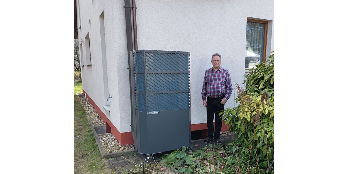Ein Mann neben einer Wärmepumpe vor seinem Haus.