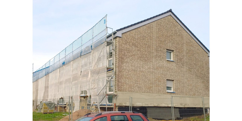 Seitenansicht des Mehrfamilienhauses in der Bauphase. Man sieht die verwitterten Klinker an der Giebelwand. Die Längsseite ist eingerüstet.