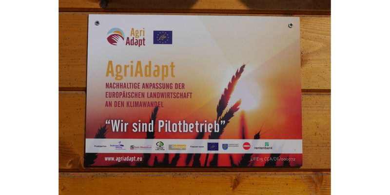 Hofschild mit Aufschrift AgriAdapt Nachhaltige Anpassung der europäischen Landwirtschaft an den Klimawandel "Wir sind Pilotbetrieb"