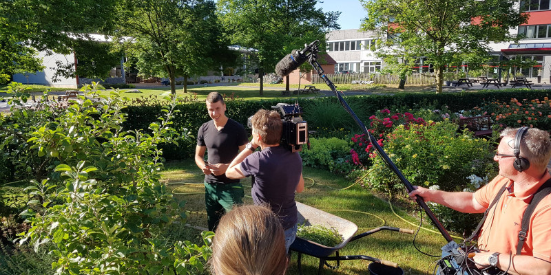 Ein Landschaftsbau-Schüler wird im Park von einem Kamerateam interviewt.