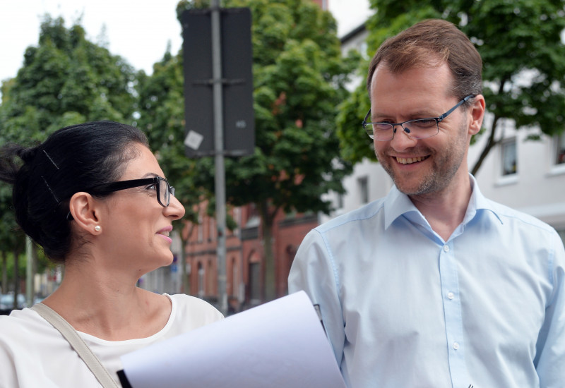 Ein Mann und eine Frau stehen sich unterhaltend und lachend nebeneinander. Die Frau hält ein Papier auf Brusthöhe.
