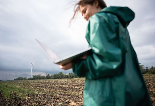 Eine Frau steht mit einem Laptop vor einer Windkraftanlage