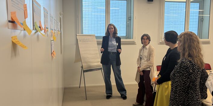 People discussing or taking note, standing in front of a wall.