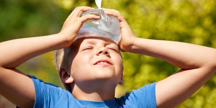 Das Foto zeigt ein Kind, das sich mit beiden Händen einen Eisbeutel zur Kühlung an die Stirn hält.