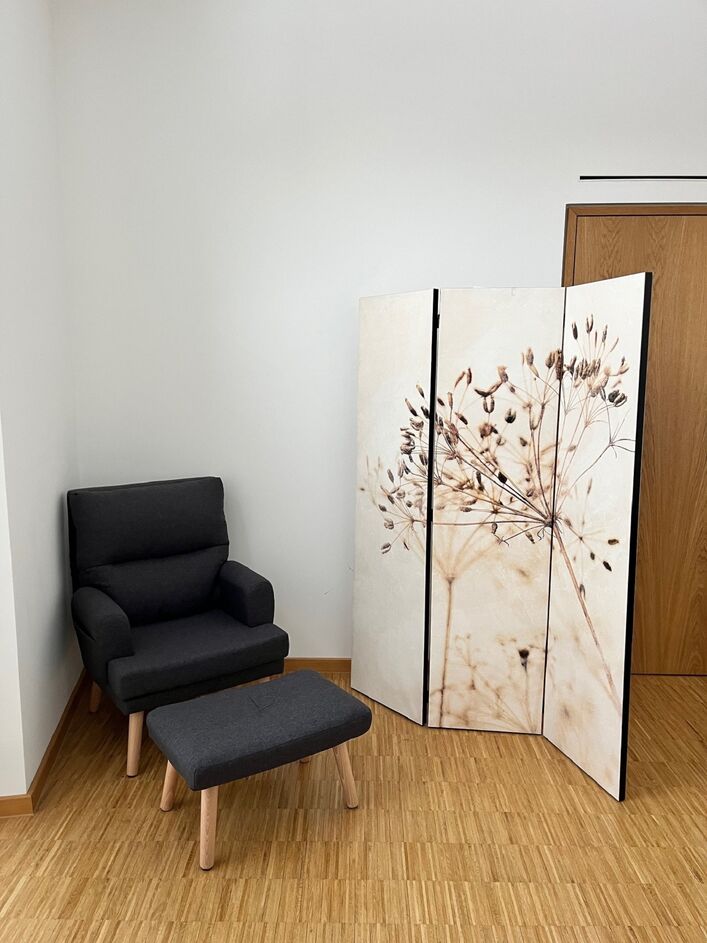 in der Ecke eines Raums steht hinter einem Sichtschutz-Paravent ein Sessel mit Möglichkeit zum Hochlegen der Füße