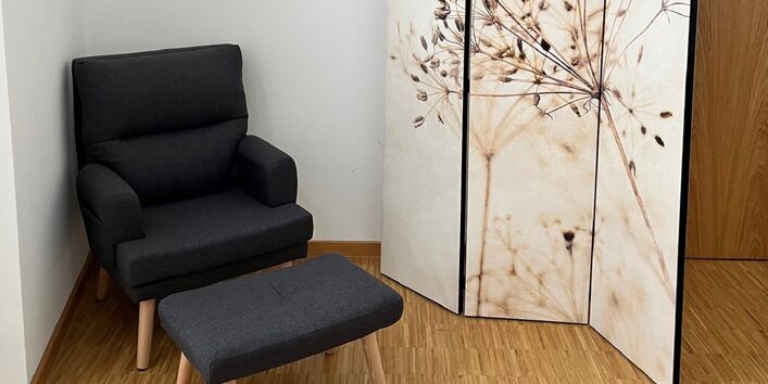 in der Ecke eines Raums steht hinter einem Sichtschutz-Paravent ein Sessel mit Möglichkeit zum Hochlegen der Füße