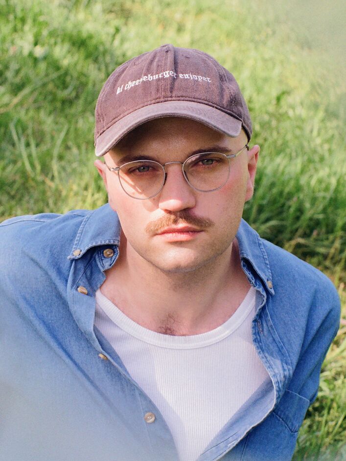 Portraitfoto Alexander Schnickmann; männlich, Brille, Bart, blaues Hemd, Basecap