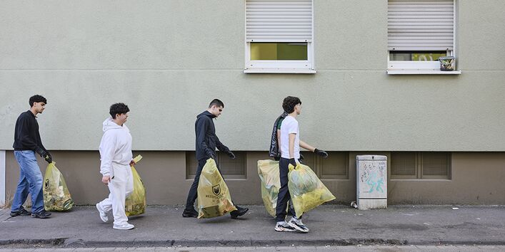 Fünf junge Männer mit Müllsäcken vor einer Häuserwand 