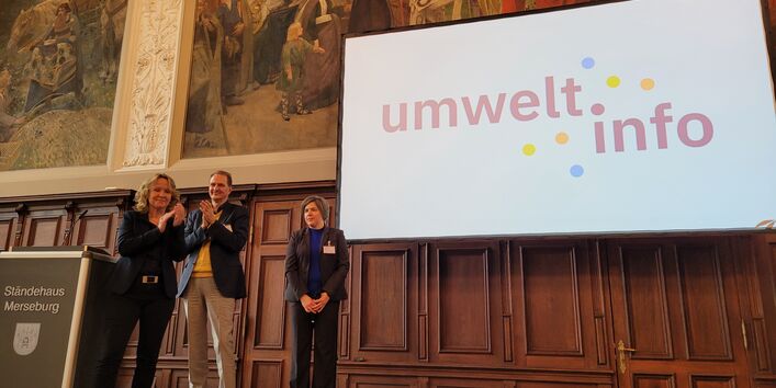 Bundesumweltministerin Steffi Lemke, UBA-Präsident Dirk Messner und xyz stehen vor einer Leinwand mit dem Logo des Portals umwelt.info.
