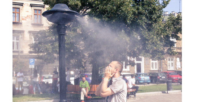 Ein Mann steht vor einem Sprühvernebeler und im Hintergrund sitzen Menschen unter einem Baum