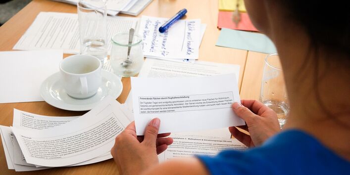 Eine Frau sitzt an einem Gruppentisch und hält eine Zettelstück