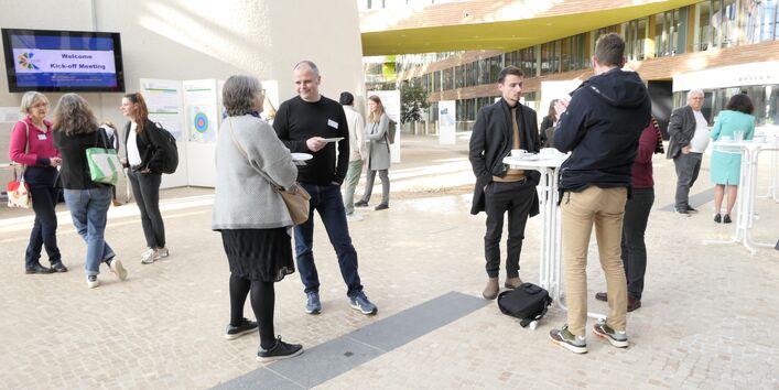 Menschen stehen in kleinen Gruppen an Stehtischen im Atrium des Umweltbundesamtes und unterhalten sich.