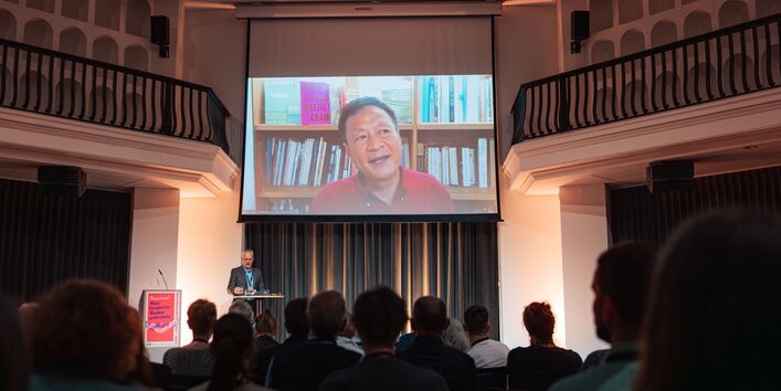 Eine Leinwand über der Bühne zeigt den Keynote Speaker.