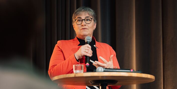 Frau Dr. Katrin Dziekan steht mit einem Mikrofon hinter einem Stehtisch auf der Bühne und spricht.