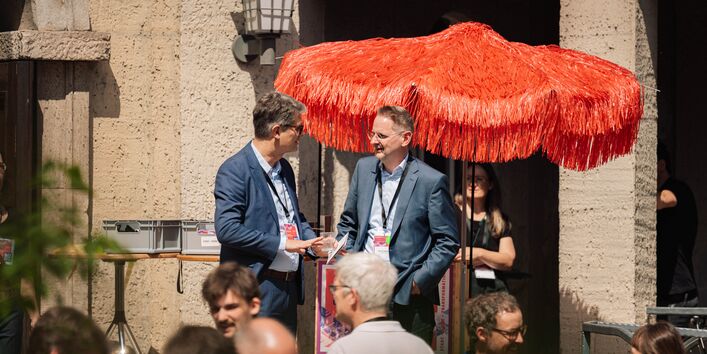 Im Fokus unterhalten sich zwei Teilnehmer. Im Vordergrund sieht man weitere TeilnehmerInnen im Austausch miteinander.