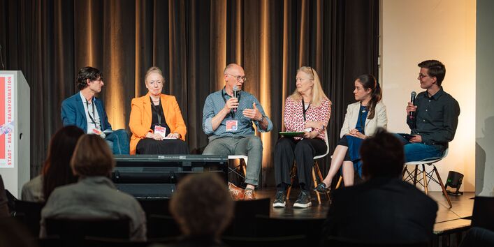 Auf der Bühne im Kuppelsaal sitzen sechs TeilnehmerInnen in einem Halbkreis auf Stühlen und befinden sich im Diskurs. Im Vordergrund sitzt das zuhörende Publikum.