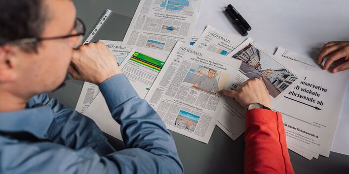 Auf einem Tisch liegen verschiedene Ausdrucke von Artikeln aus den Medien. Teilnehmerinnen sitzen drum herum und besprechen die unterschiedlichen Berichte.