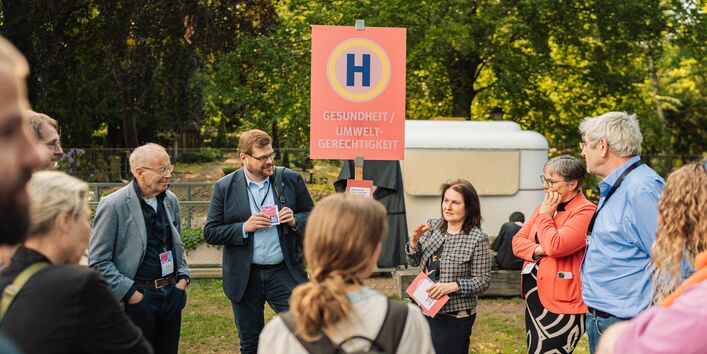 Am Schild mit der Aufschrift „Gesundheit/Umweltgerechtigkeit“ sprechen Konferenzteilnehmende.