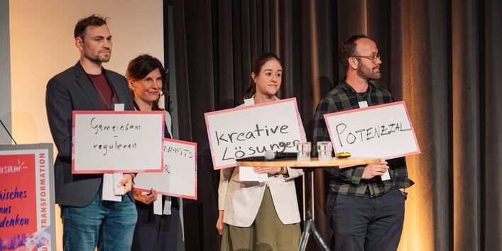 Vier Personen stehen auf der Bühne und halten Schilder mit Schlagwörtern vor sich.