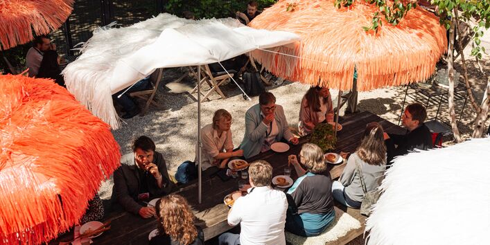 Teilnehmende sitzen gemeinsam an einem Holztisch im Außenbereich und essen.