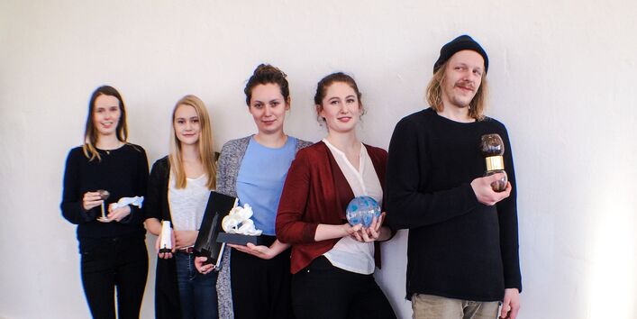 vier junge Frauen und ein junger Mann mit Trophäen in der Hand an eine Wand gelehnt