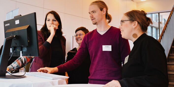 ein Mann und drei Frauen schauen auf einen Computermonitor