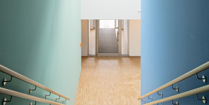 Treppe abwärts mit Holz-Handläufen, die rechts Wand ist blau, die linke in einem hellen grün-blau gestrichen