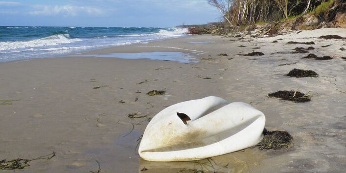 kaputter weißer Gymnastikball liegt, ähnlich einem Schwan, an einem Sandstrand am Meer