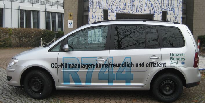 silbergraues Auto mit der Aufschrift "CO₂-Klimaanlagen - klimafreundlich und effizient, R744" und dem Logo des Umweltbundesamtes