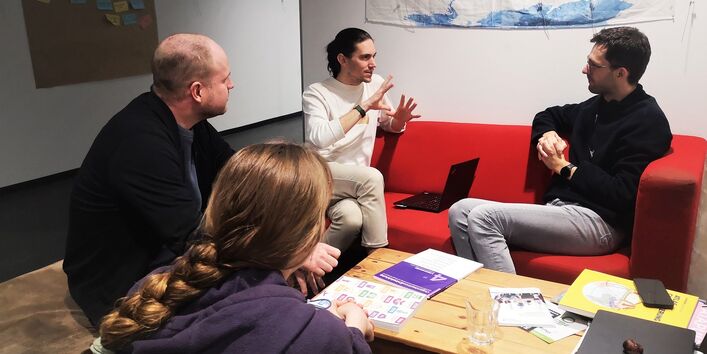 drei Männer und eine Frau sitzen um einen Tisch und diskutieren Fragestellungen