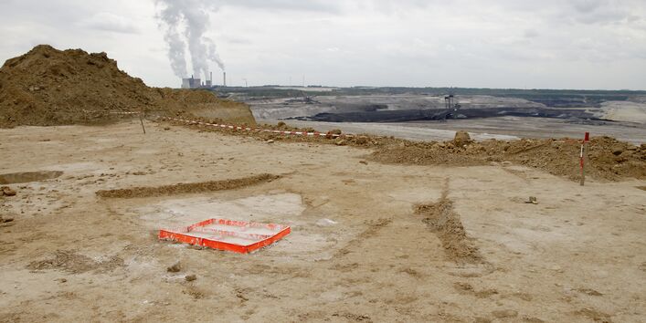 Eine karge Bergbau Landschaft, im Hintergrund eine Energieanlage, vorne sieht man den roten Rahmen, mit dem die Künstlerin einen Bodenabdruck macht.