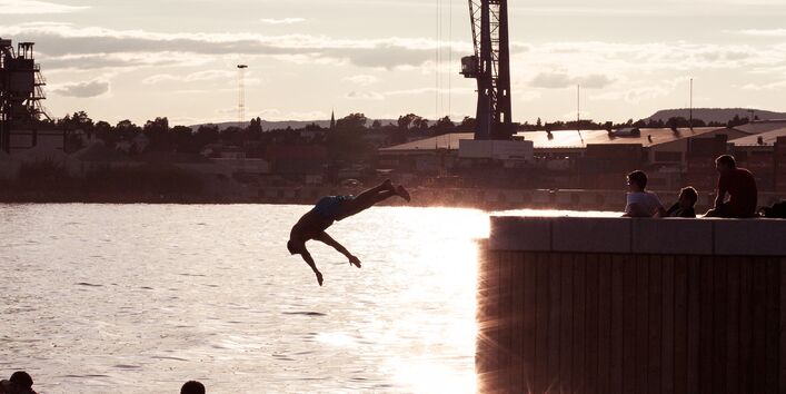 Im Hafen von Oslo: Bei untergehender Sonne springt ein Mann von einem Steg ins Wasser, davor sieht man zwei Personen, die in der Abendsonne sitzen.