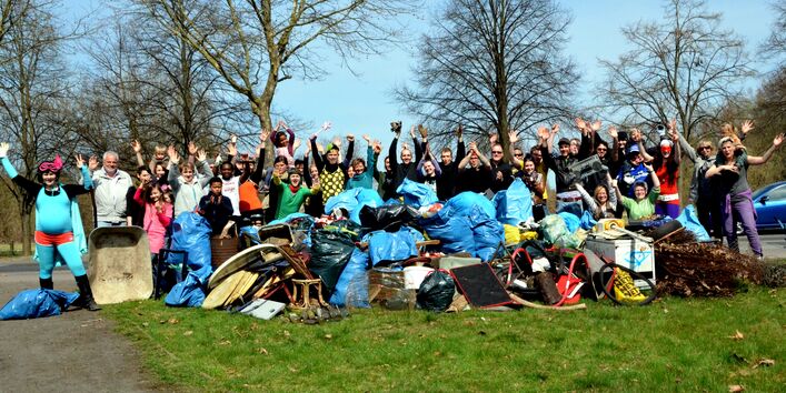 Gruppenfoto von etwa 30 Personen nach einer Müllsammelaktion im Wald und freien Feld. Einige Personen sind verkleidet, im Vordergrund liegt der gesammelte Müll.