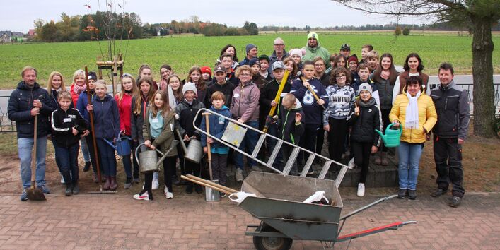 Das Bild ist ein Gruppenfoto mit Kindern und Helfer*innen, die an einer Begrünungsmaßnahme für den Schulhof der Grundschule Wahrenbrück beteiligt sind.