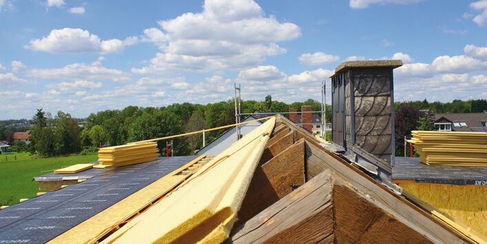 Das Bild zeigt einen abfedeckten Dachstuhl, auf dessen linker Seite Dämmmaterial verlegt wurde.