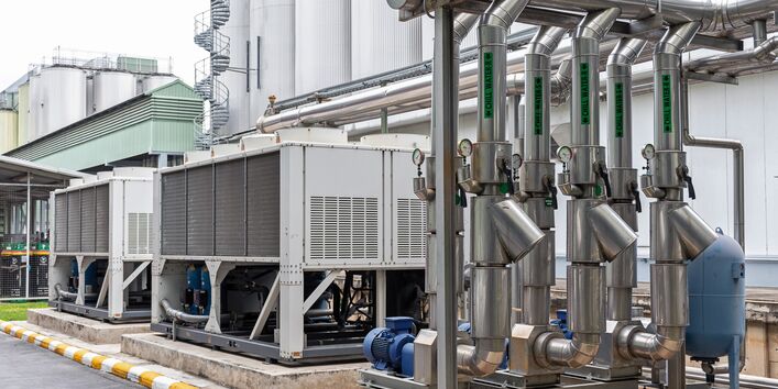 The picture shows a pipeline system in front of industrial plant used for feeding cold water into a production process. Apart from the pipes, there are other technical assemblies visible. 