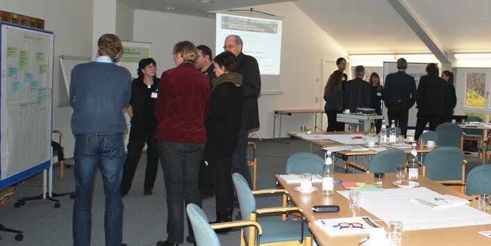 Teilnehmer stehen im Workshopraum in Grüppchen vor den Moderationswänden im Dialog miteinander.