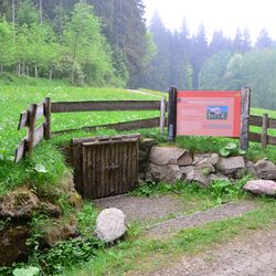 Ein Bodenprofil hinter einem Holztor und eine Tafel daneben