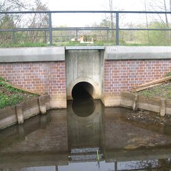 Auf dem Foto ist die Verrohrung eines Bachs unter einer Brücke dargestellt