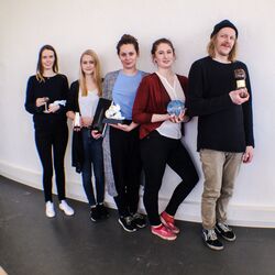 vier junge Frauen und ein junger Mann mit Trophäen in der Hand an eine Wand gelehnt