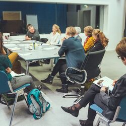 Gruppe von diskutierenden Teilnehmern im Hintergrund, schräg davor eine weitere Person