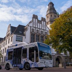 Ein mit Wasserstoff betriebener Kleinbus steht auf der Straße vor einem alten Gebäude und einem Baum