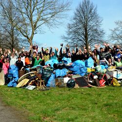 Gruppenfoto von etwa 30 Personen nach einer Müllsammelaktion im Wald und freien Feld. Einige Personen sind verkleidet, im Vordergrund liegt der gesammelte Müll.