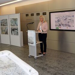 Staatsministerin Ulrike Scharf an einem Rednerpult. Um sie herum die ausgestellten Fotografien.