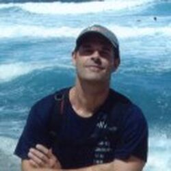 Ein Foto des Künstlers Sven Hoffmann lächelnd mit verschränkten Armen vor reißendem Wasser stehend.