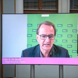 Auf einem flachen Bildschirm im hellen historischen Innenhof ist im Großformat zu sehen wie der Präsident des Umweltbundesamts einen Beitrag spricht.