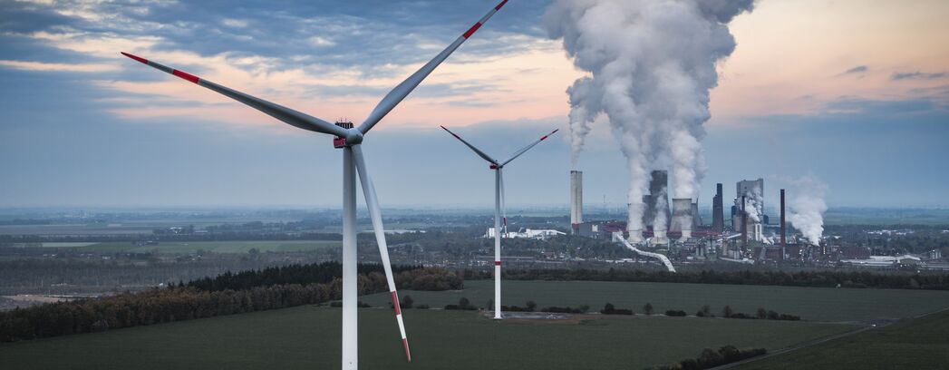 Landschaft mit Windrädern und Kraftwerk, aus dem Rauch aufsteigt