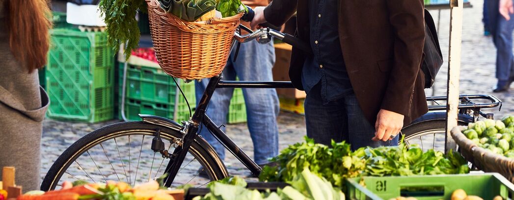 Ein Mann kauft auf einem Wochenmarkt mit seinem Fahrrad Gemüse ein