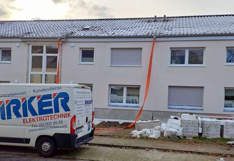 Ein breites, zweistöckiges Mehrfamilienhaus. Es sind zwei Hauseingänge zu sehen, die Bauarbeiten sind noch nicht abgeschlossen. Ein Lieferwagen steht vor dem Haus.