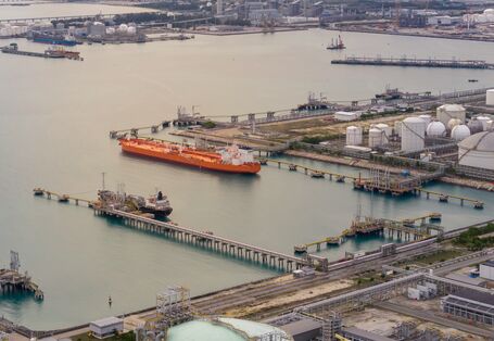 Großer, roter Öltanker an einem Raffinerieterminal mit weißen Lagertanks, Pipelinenetzwerken und Offshore-Ladeplattformen